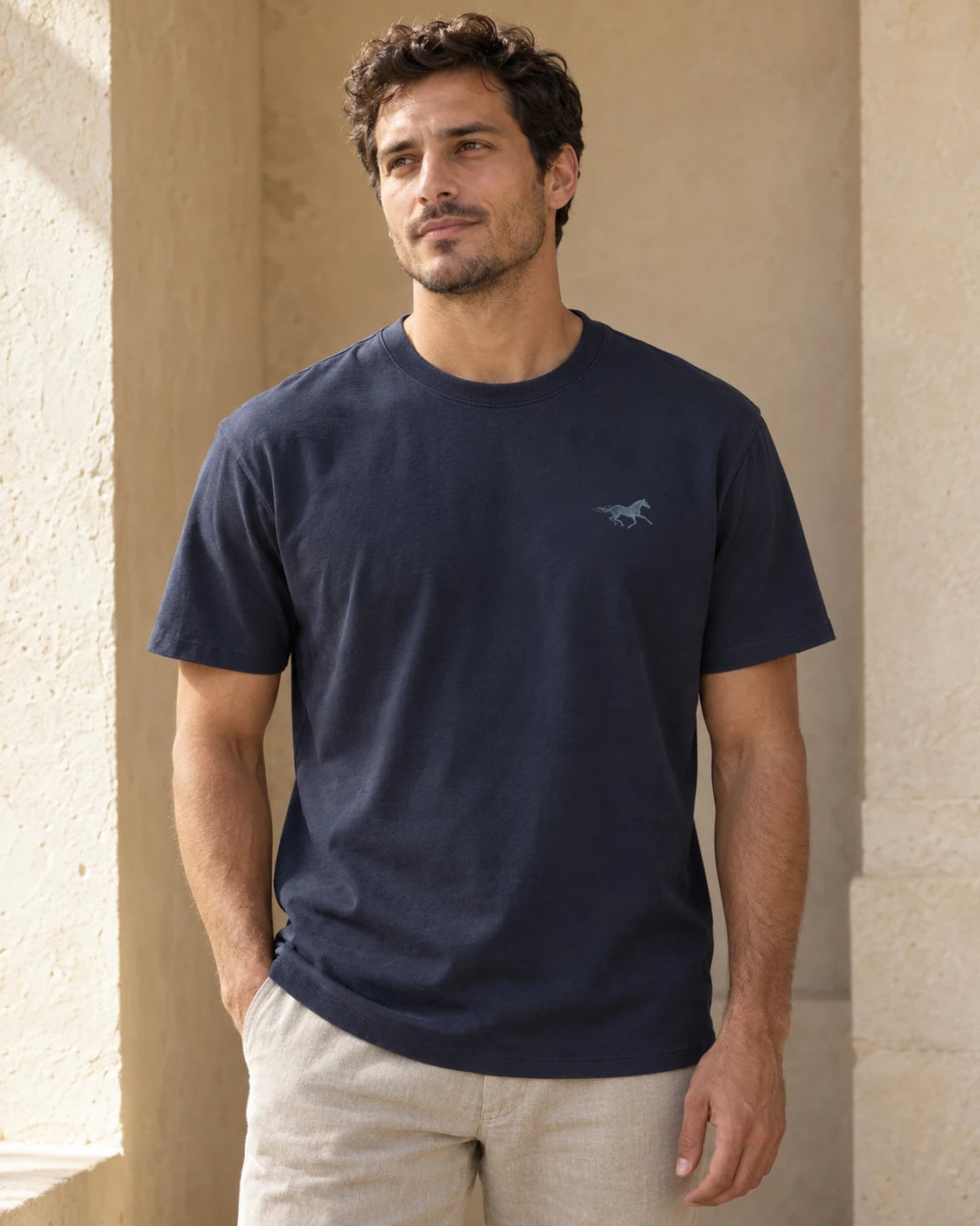 Person wearing a dark navy Floreo T-shirt with a small pale blue horse chest mark in warm daylight. Concept image.